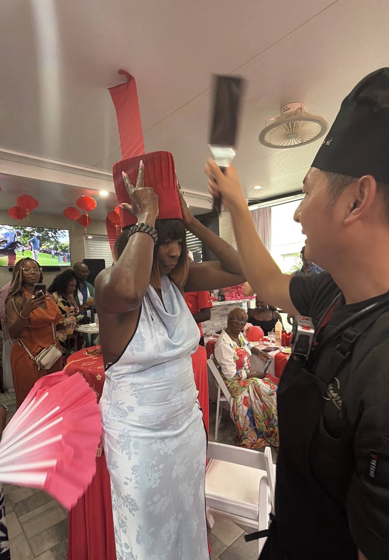 Hibachi chef playfully placing a tall red chef hat on a smiling guest at a private party in Nocatee, Florida
