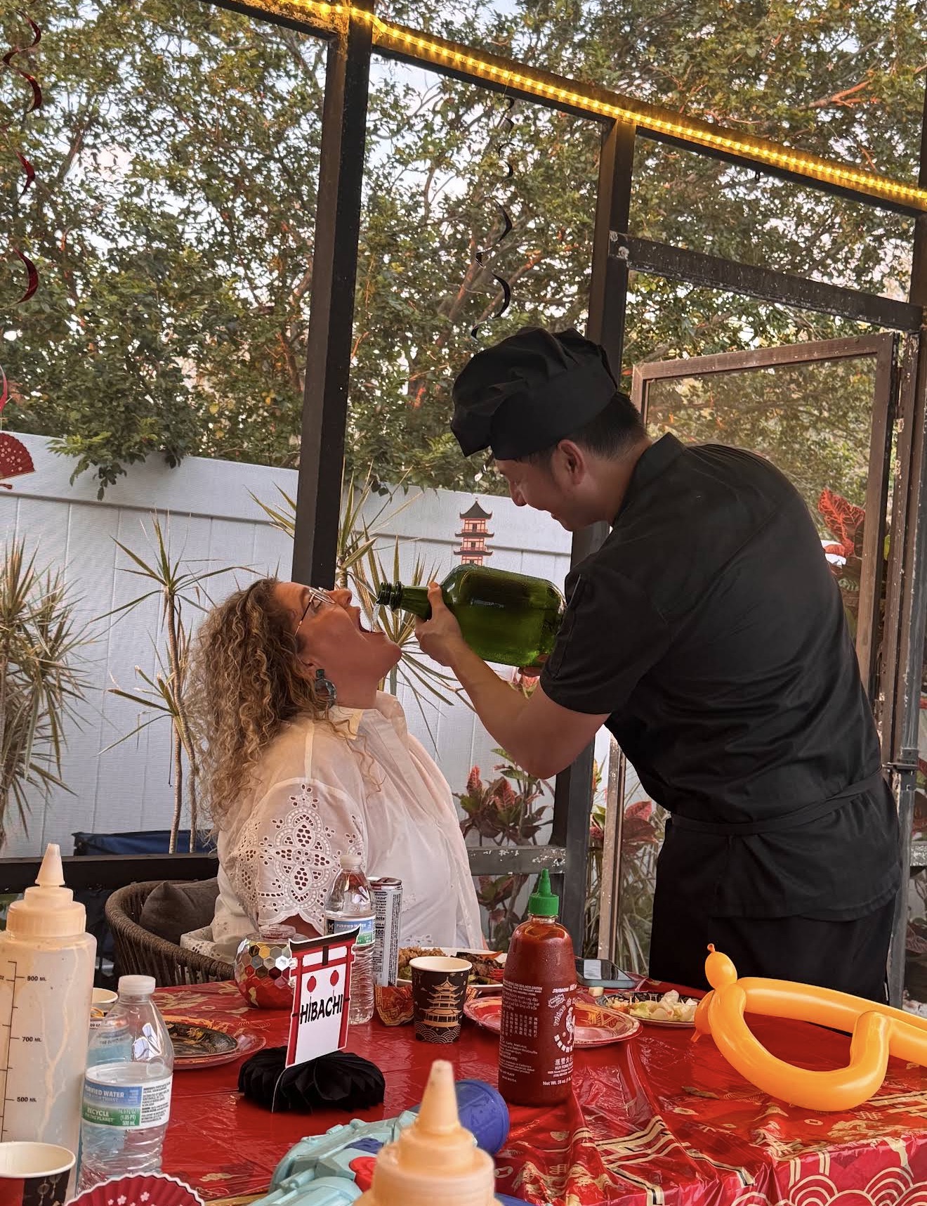 Hibachi chef performing a sake pour trick for a laughing guest at an outdoor private party in Apollo Beach, Florida
