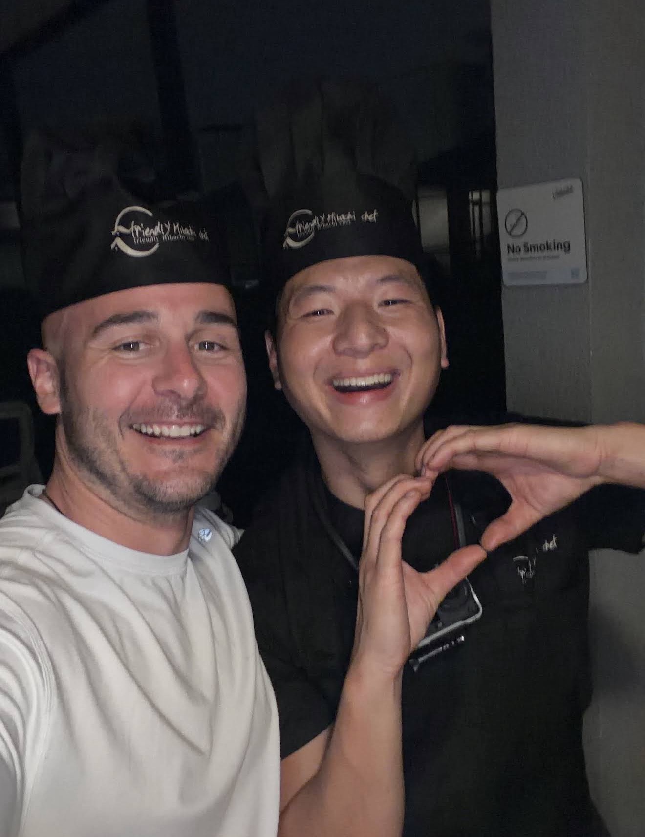 Friendly hibachi chef taking a happy selfie with a guest, making a heart gesture, in Fernandina Beach, Florida
