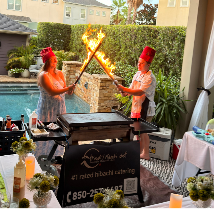 Two people crossing flaming torches while wearing red chef hats at a poolside hibachi party in Southwest Florida