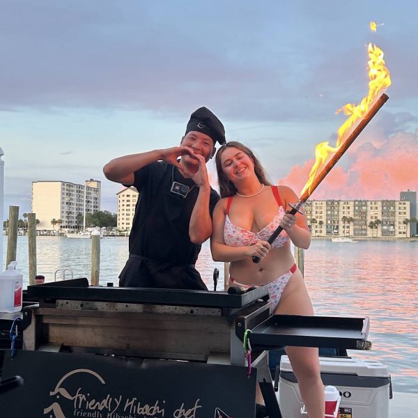 Hibachi chef and a guest holding a flaming torch at sunset by the water in Clearwater Beach, Florida