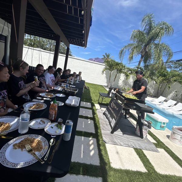 Guests seated at a long outdoor table watching a hibachi chef cook by the pool in Clearwater Beach, Florida