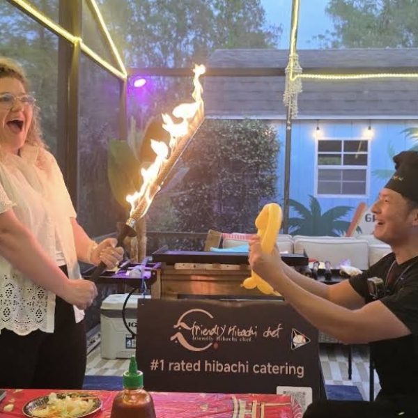 Hibachi chef and a laughing guest holding flaming torches together at a poolside party in Fort De Soto, Florida