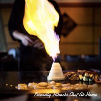 Onion volcano fire trick with flames on the hibachi grill beside grilled steak and vegetables