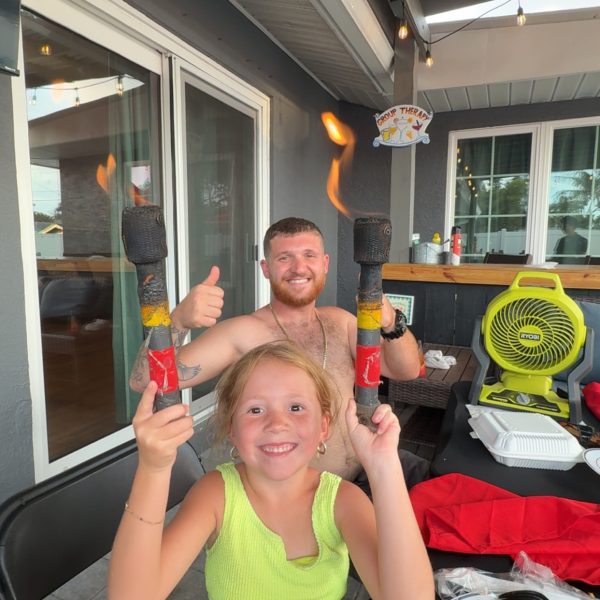 A young girl happily holding two flaming torches at a family hibachi party in Southwest Florida